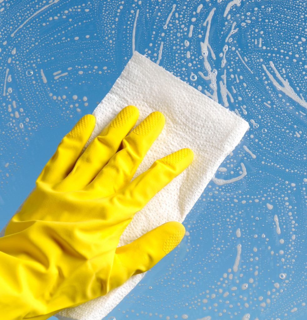 Cleaning a glass surface with yellow gloves on, cleaner and paper towel.
